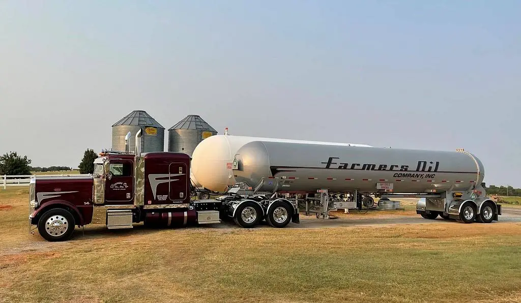 Maroon Farmers Oil Peterbilt and propane transport in front of grain bins on the plains