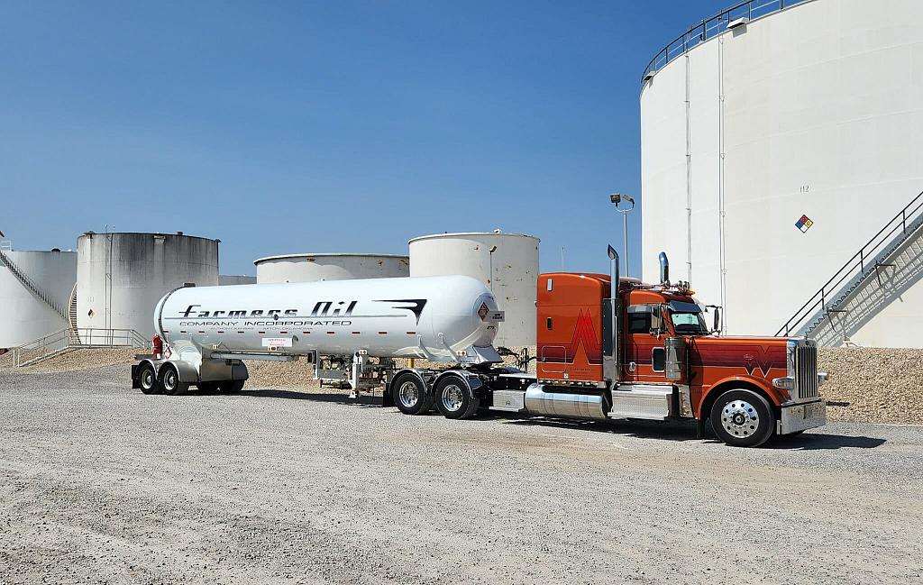 Orange Farmers Oil Peterbilt and white propane transport beside large white storage tanks
