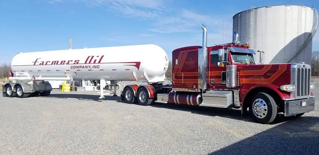Red Farmers Oil Peterbilt hooked to a white propane transport beside a large storage tank