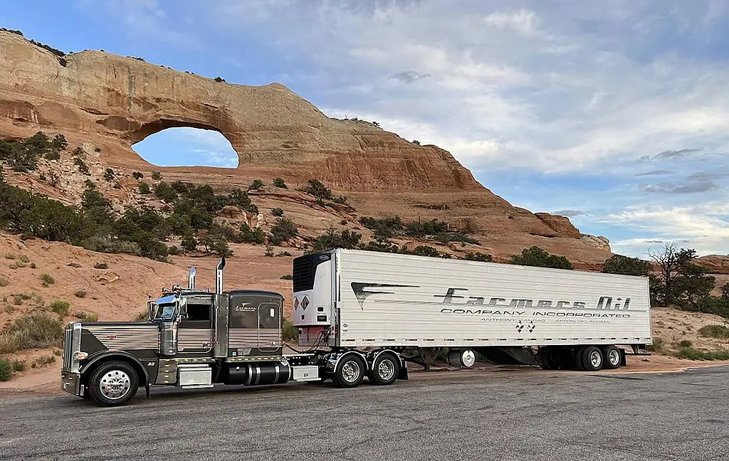 Farmers Oil truck and white refrigerated trailer beneath a red sandstone arch