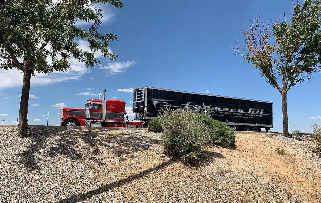 Red Farmers Oil Peterbilt and black refrigerated trailer in a desert landscape