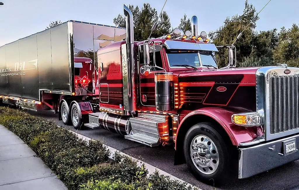Maroon Farmers Oil Peterbilt with glowing marker lights pulling a polished refrigerated trailer at dusk