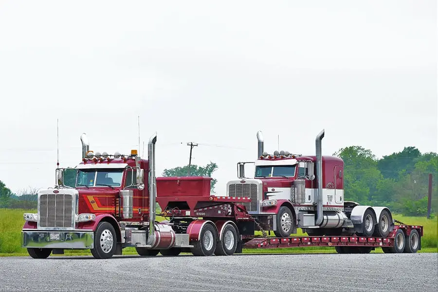 Two red Farmers Oil Peterbilts with a lowboy trailer