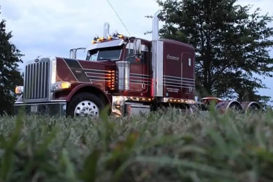 Maroon Farmers Oil Peterbilt photographed low through tall grass