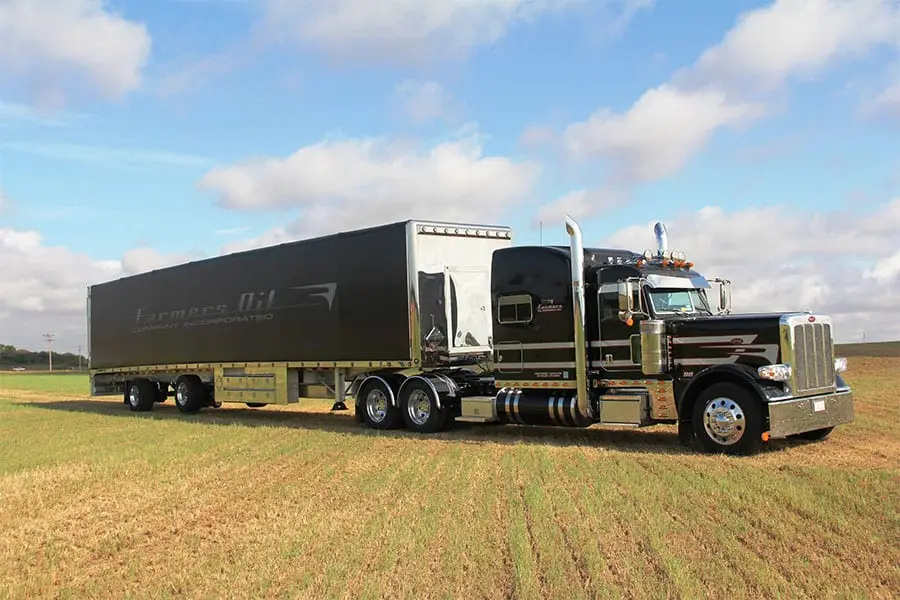 Black Farmers Oil Peterbilt and black van trailer in a green field